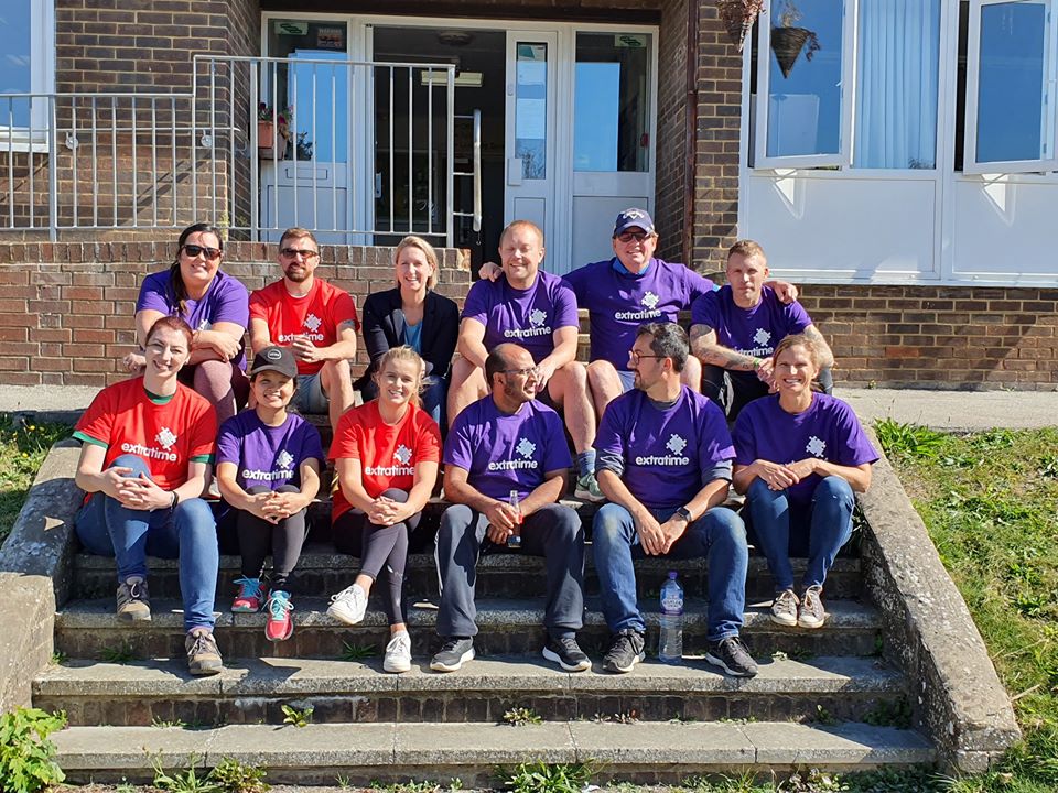 12 people sat in two rows on a set of stairs wearing Extratime t-shirts at Portslade Village Centre