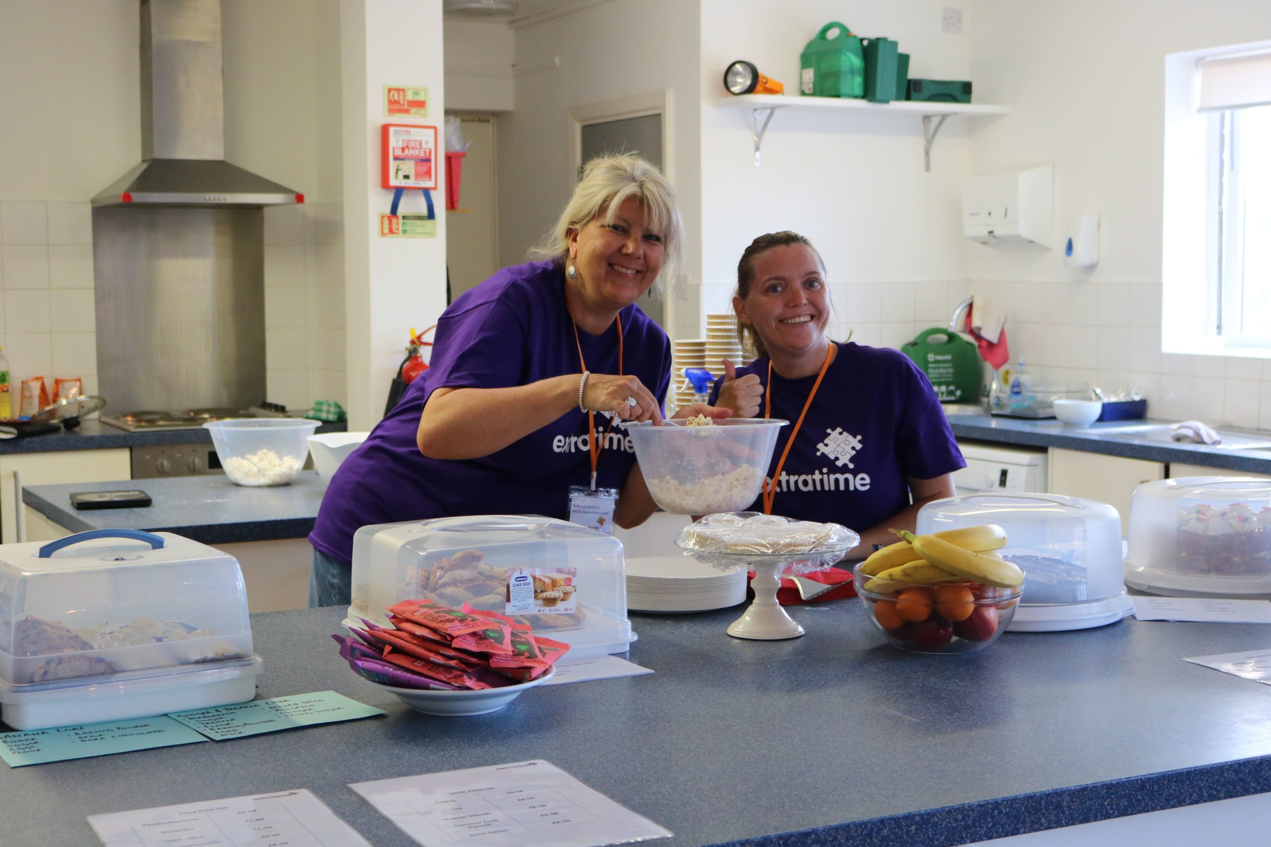 Two females posing with a selection of food for sale